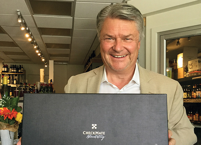 Ingo Grady, Director of wine education at CheckMate, holds a three bottle case of CheckMate